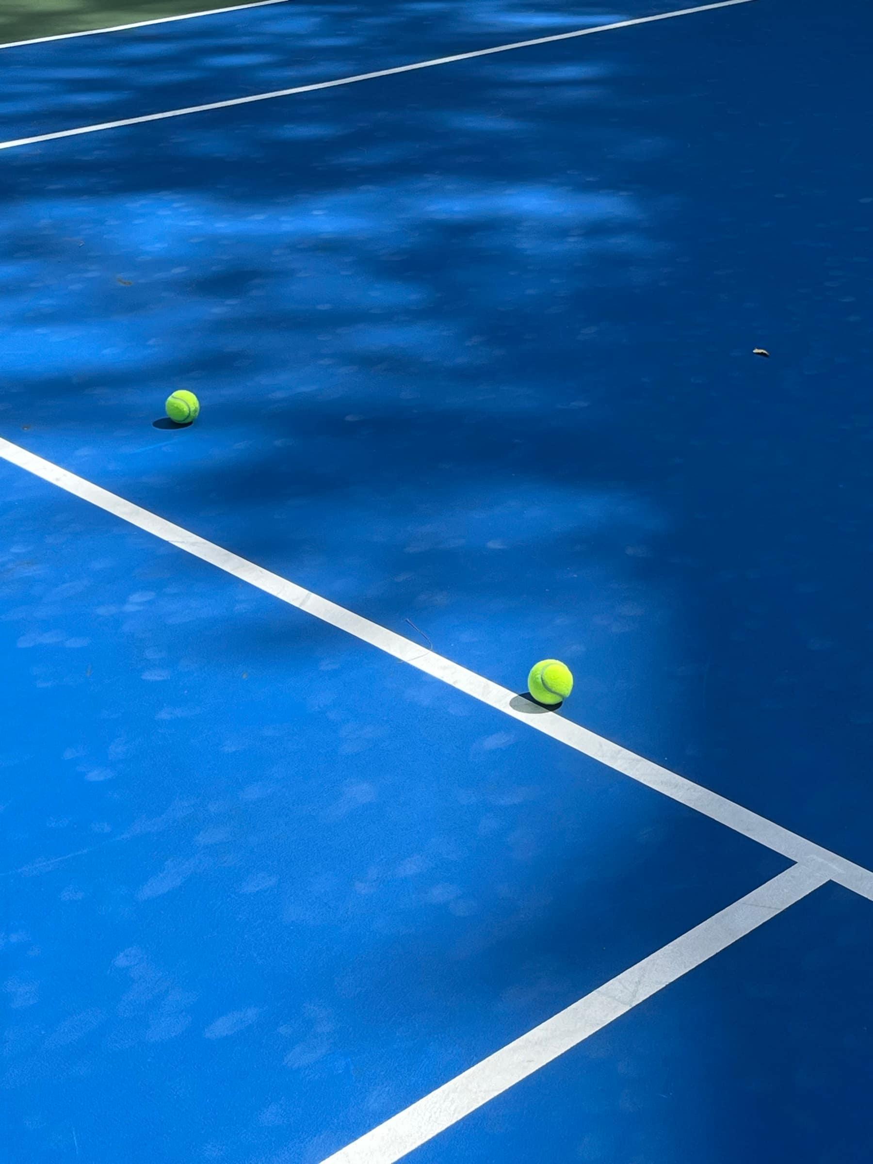 Tennis balls resting on the white lines of a sunlit blue hard court